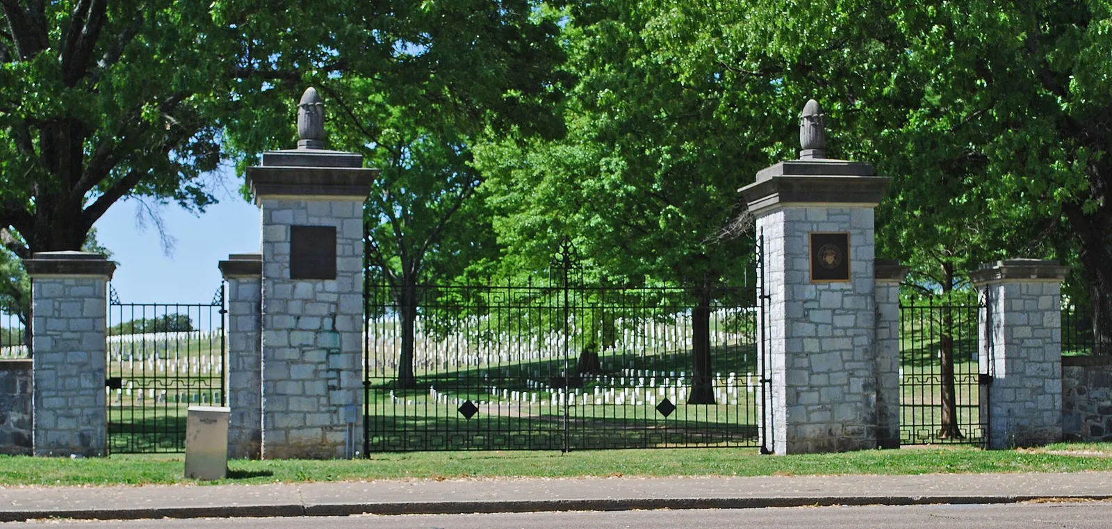 The stone and iron entrance gates of Chattanooga National Cemetery, with rows of headstones beyond.