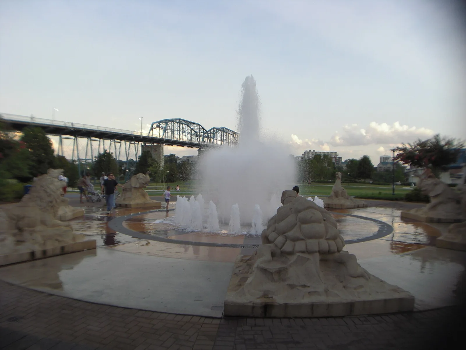 Children play in the interactive fountain at Coolidge Park, with the Walnut Street Bridge behind.